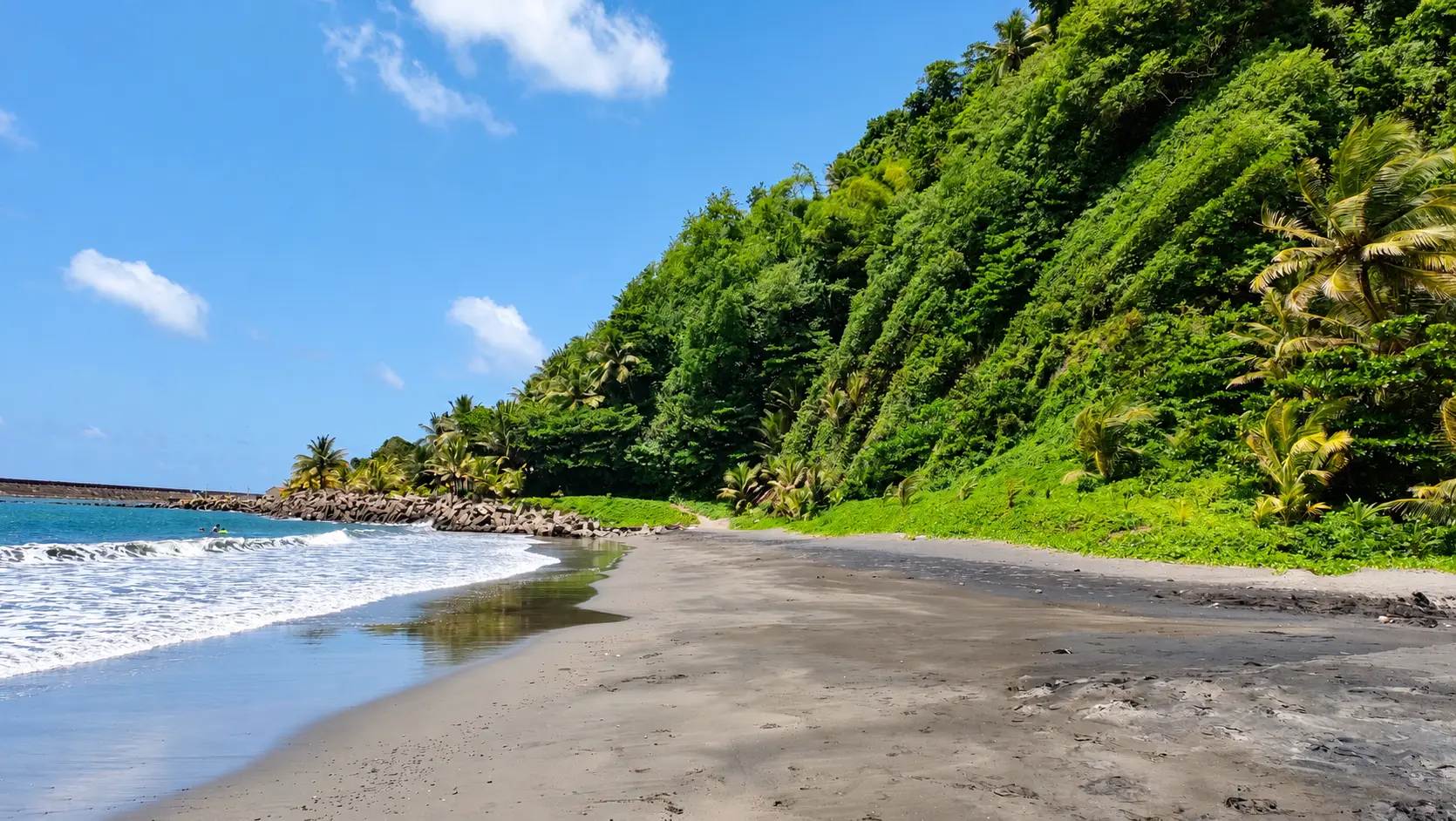 Plage de sable noir au pied d’un versant couvert de végétation tropicale